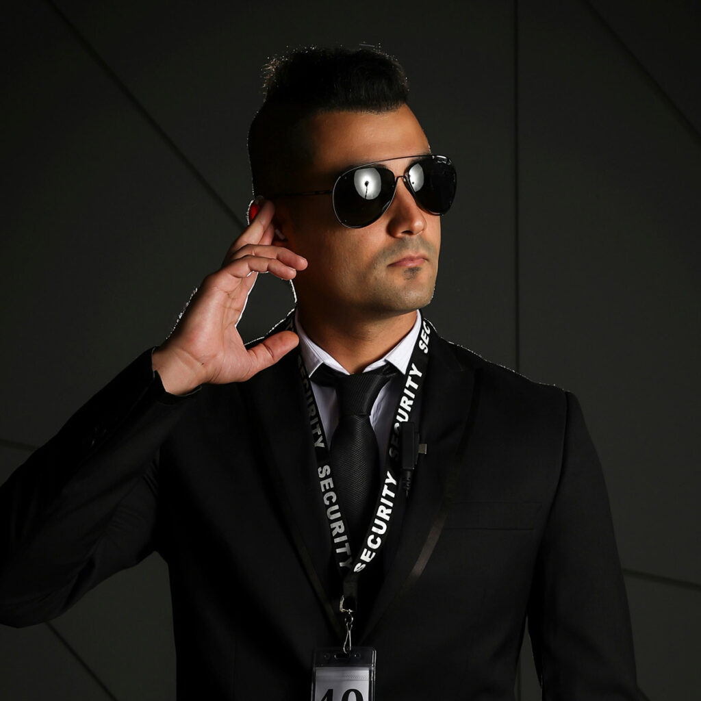 Security guard in a suit and sunglasses, using an earpiece, demonstrating professionalism and readiness for armed or unarmed security duties.