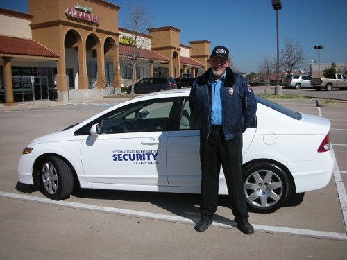 Security officer standing next to a white patrol car with "SECURITY" branding, outside a commercial building, representing International Security Services' patrol services.