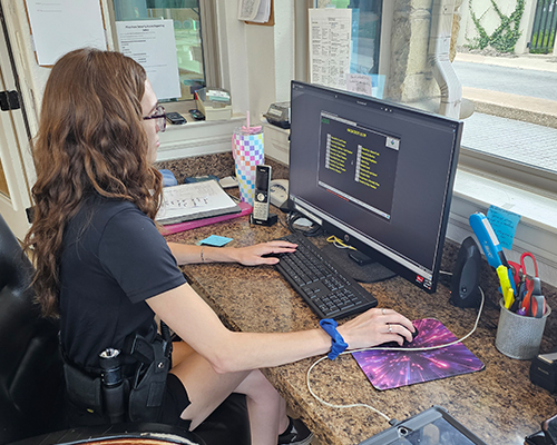 Security officer at desk using computer for visitor pass issuance and credential checks in gated community.