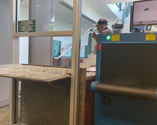 Security checkpoint with automated screening system, officer monitoring procedure, and visible signage for safety protocols.