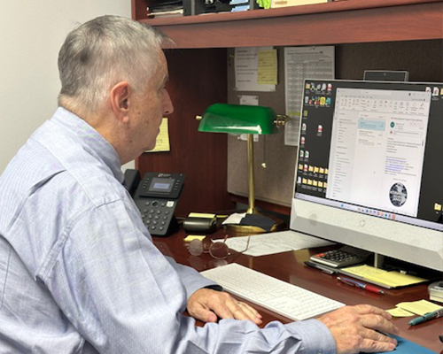 Man working at a desk with a computer, engaged in administrative tasks related to security services for residential communities.