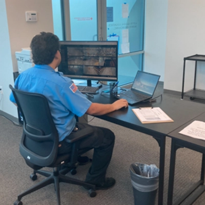 Security officer monitoring surveillance feeds at a desk with multiple screens, emphasizing access control and community safety in a residential environment.